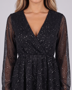 Women's black sparkly mini dress with glitter stars, V-neck and long sleeves in sheer mesh, close-up of the wrap bodice and glitter stars
